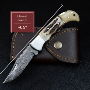May include: A small pocket knife with a damascus steel blade and a stag horn handle. The knife is closed and has a leather sheath. The overall length of the knife is approximately 6.5 inches.