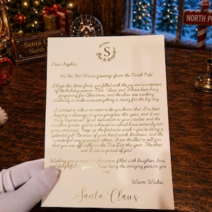 May include: A white letter from Santa Claus featuring a gold foil letterhead with the letter S inside a wreath. The text is written in a cursive font and addresses Sophia, mentioning the North Pole, Christmas, and her inclusion on the Nice List.