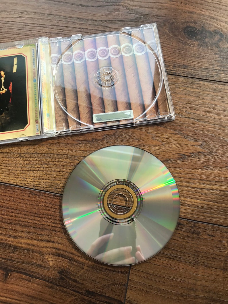 May include: A clear CD case containing cigars, alongside a silver CD. The cigars are brown and neatly arranged. The CD has a reflective surface, showing rainbow hues.