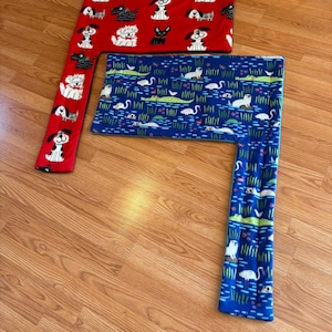 May include: Two fleece pet bed covers. One is red with white and black dog illustrations. The other is blue with a pattern of white swans, green alligators, and aquatic plants. Both are rectangular with an attached side.