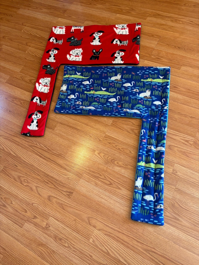 May include: Two fleece pet bed covers. One is red with white and black dog illustrations. The other is blue with a pattern of white swans, green alligators, and aquatic plants. Both are rectangular with an attached side.