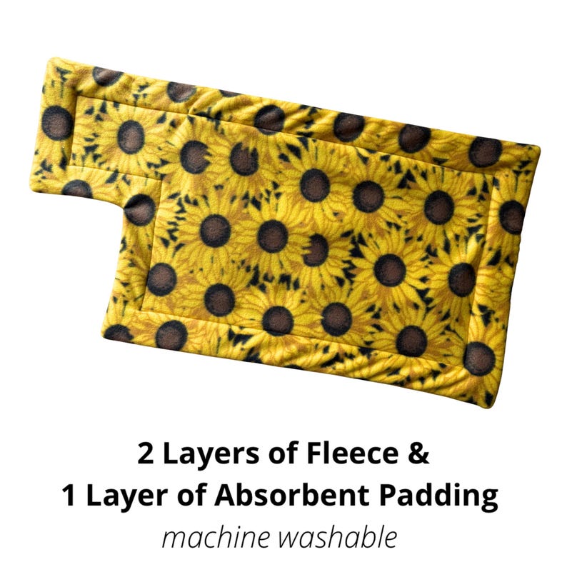 May include: A rectangular, yellow fleece pad with a sunflower pattern. The pad has a unique shape with a small extension on one side. Text on the image reads: "2 Layers of Fleece & 1 Layer of Absorbent Padding machine washable."
