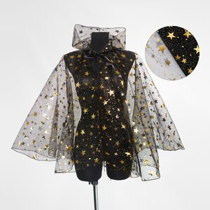 May include: A black cape with gold star patterns, displayed on a mannequin. The cape features a high collar and a bow at the neckline. The fabric is sheer, allowing the mannequin's form to be partially visible. A close-up shows the fabric's texture.