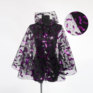 May include: A black cape with a hood, adorned with purple bat and star shapes. The cape is made of sheer fabric and tied at the neck with a black ribbon. A smaller, circular image shows the fabric's pattern.