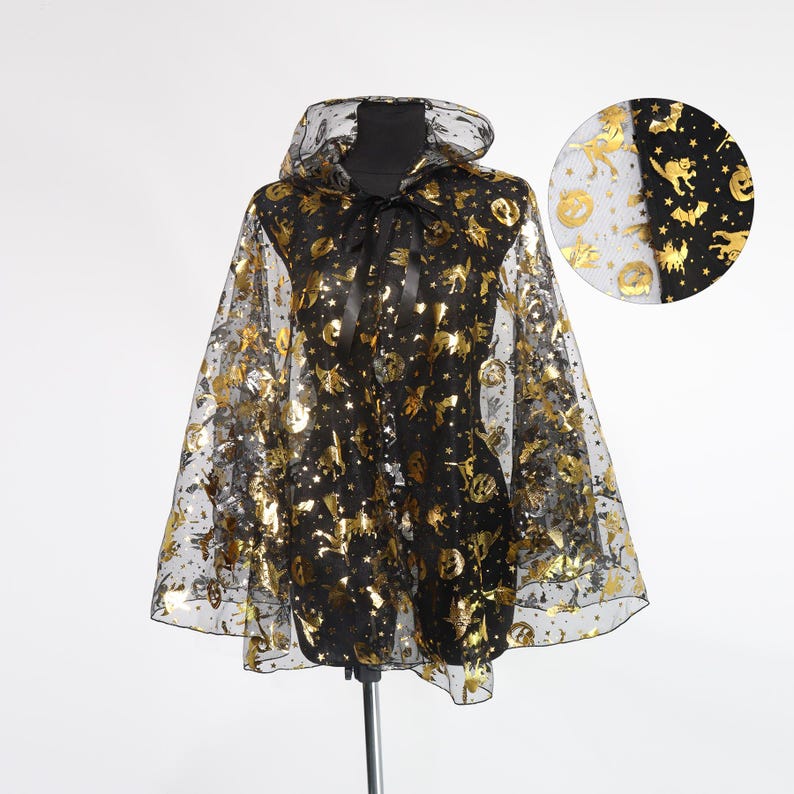 May include: A black Halloween cape with a hood, adorned with gold foil images of bats, cats, stars, and pumpkins. The cape is sheer, allowing the black fabric underneath to show through. A black ribbon ties at the neck.