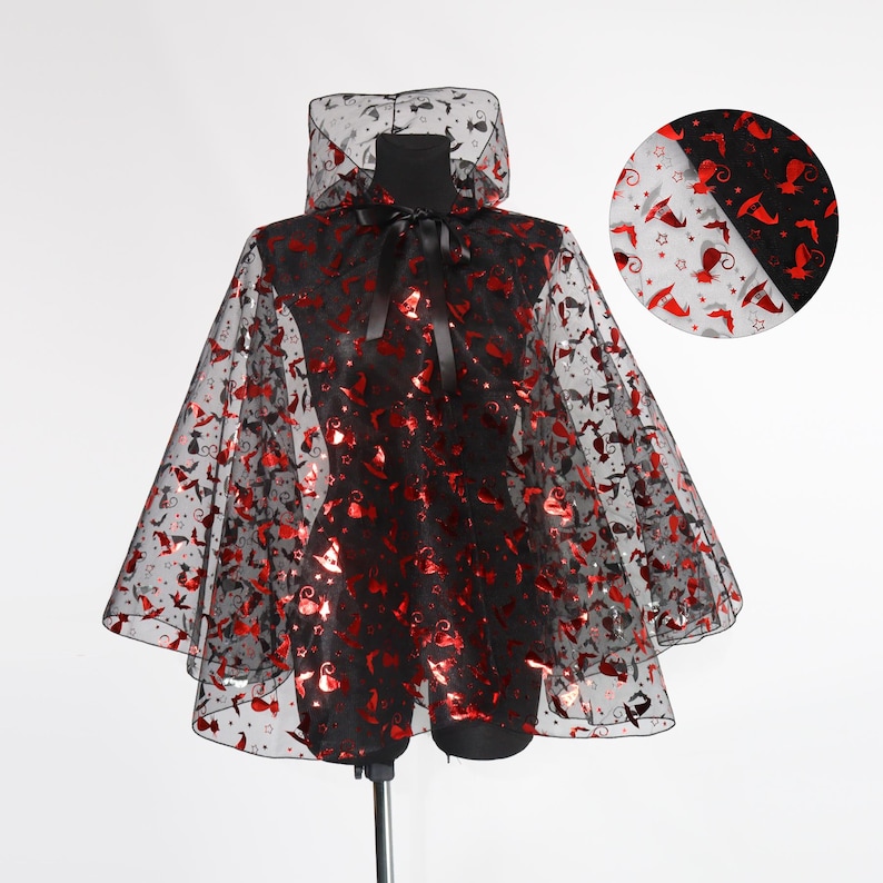 May include: A black cape with a hood, adorned with red glittery shapes of bats, witch hats, and stars. The cape has a black ribbon tie at the neck and is displayed on a mannequin. The cape is made of a sheer material.
