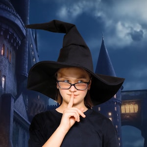 May include: A person wearing a black witch hat and glasses, with a finger over their lips. The background features a castle under a cloudy sky. The hat has a wide brim and a tall, pointed crown.