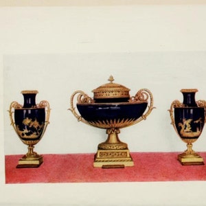 Op de afbeelding: Drie decoratieve vazen met gouden accenten en blauwe en gouden beschilderde ontwerpen. De middelste vaas is groter en heeft een deksel.