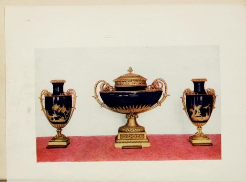 Op de afbeelding: Drie decoratieve vazen met gouden accenten en blauwe en gouden beschilderde ontwerpen. De middelste vaas is groter en heeft een deksel.