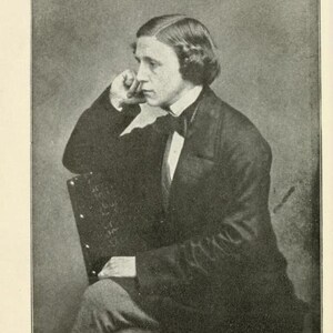 May include: A black and white portrait of Lewis Carroll, a man with a mustache and a bow tie, sitting in a chair with his hand on his chin.