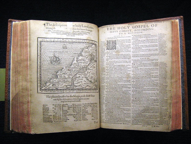 May include: An antique book with a map of the Holy Land and text from the Holy Gospel of Jesus Christ according to St. Matthew. The book has a brown leather cover and is open to a page with a map and a list of places.