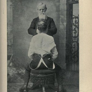 May include: A black and white photo of two men. The man in the foreground is sitting on a stool with his back to the camera. The man in the background is standing and holding the seated man's shoulders. The photo is captioned "Plate XLV. - Method of Stimulating Vaso-motor Nerves."