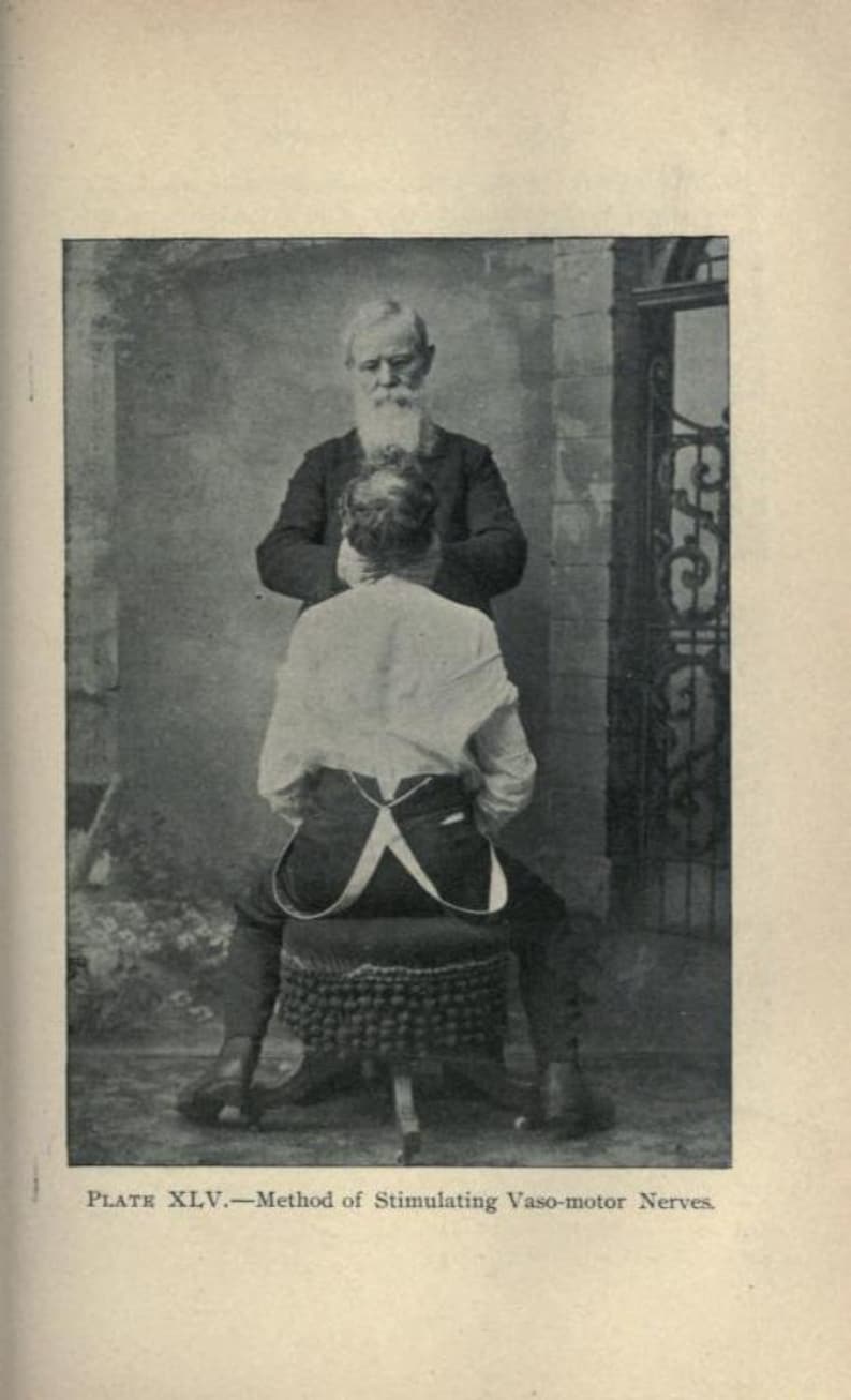 May include: A black and white photo of two men. The man in the foreground is sitting on a stool with his back to the camera. The man in the background is standing and holding the seated man's shoulders. The photo is captioned "Plate XLV. - Method of Stimulating Vaso-motor Nerves."