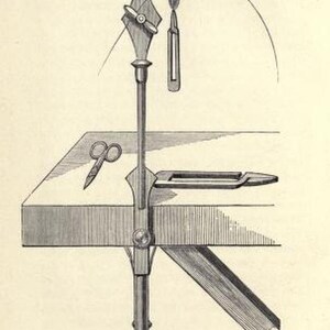 May include: A black and white illustration of a fly tying vise, a tool used to hold a hook while tying a fly. The vise is mounted on a wooden base and has a lever to tighten the hook. A fly is shown tied to the hook, and a pair of scissors are on the base.
