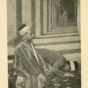 May include: Two men are kneeling in prayer in a mosque. The man in the foreground is wearing a white turban and a long robe. The man in the background is wearing a white turban and a long robe. The mosque is decorated with intricate tile work.