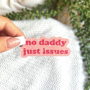 May include: Pink sticker with a white outline and glitter. The sticker says "no daddy just issues" in red letters.