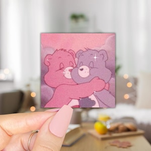May include: Two pink and purple cartoon bears hugging each other against a pink and white background with glitter accents.