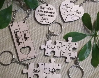 May include: Set of wooden keychains with engraved text. One keychain is a heart shape with the text "Mana Anais" and the date "71.91.04->". Another keychain is a round shape with the text "Aujourd'hui Je t'aime Depuis 1843 Jours". A third keychain is a rectangular shape with the text "Christophe Emilie" and the date "04.11.08 01.11.08". The last keychain is a puzzle piece shape with the text "18.02.17" on each piece.
