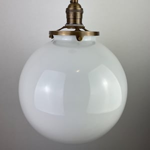 May include: A white glass globe pendant light fixture with a brass socket and a brass ring around the top of the globe.