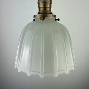May include: A white frosted glass pendant light with a brass fixture and a ribbed design. The light has a scalloped edge.