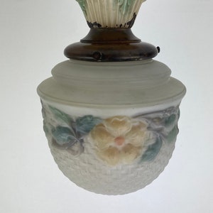 Może przedstawiać: Antyczna lampa sufitowa z białym, matowym kloszem ze szkła, ozdobionym wzorem kwiatowym i plecionym koszem. Lampa ma ozdobną metalową podstawę z kwiatowymi akcentami w odcieniach zieleni, żółci i różu.