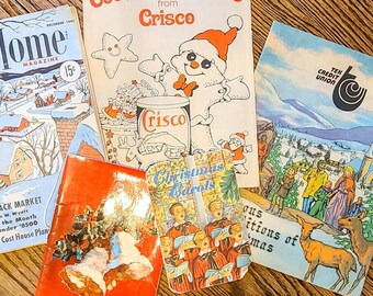May include: A collection of vintage Christmas-themed magazines and pamphlets. The magazines feature images of a snowman, carolers, and a winter scene. The pamphlets include a Christmas cookie recipe from Crisco and a Christmas carol book.