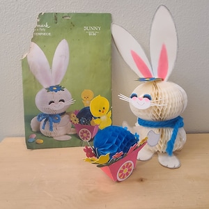May include: A white paper mache bunny with blue ribbon and a blue paper mache egg in a pink wagon with yellow flowers. The bunny is holding a blue paper mache egg. The bunny is 12 inches tall and the egg is 6 inches tall. The bunny is a craft kit from Hallmark.