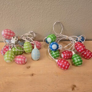 May include: A string of Easter egg lights with a white cord. The eggs are made of plastic and have a checkered pattern in pink, green, blue, and white.