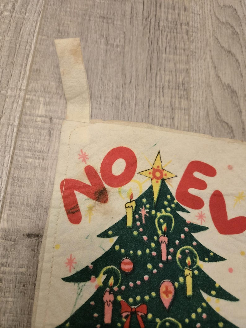 May include: A vintage Christmas stocking with a green Christmas tree and the word "NOEL" in red letters. The stocking is made of white fabric with a red and white trim.