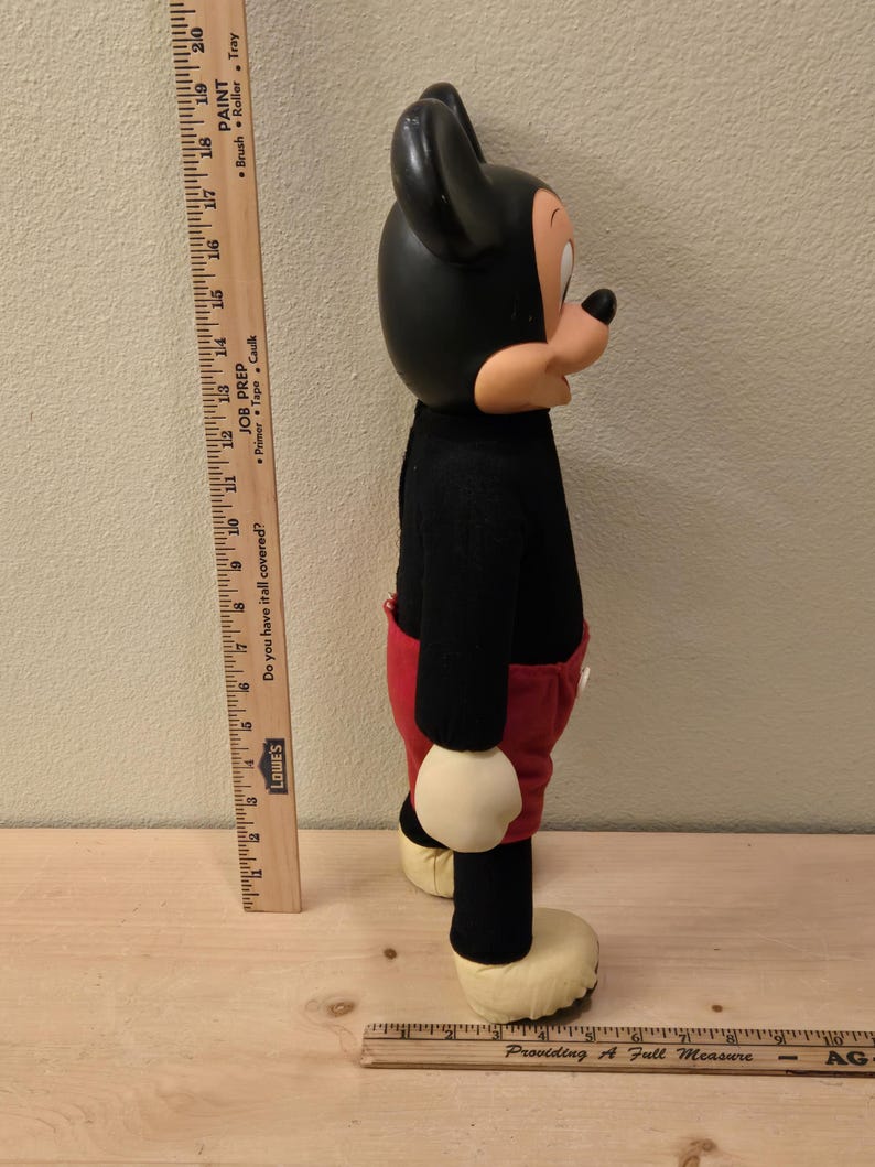 Peut inclure: Une poup&eacute;e en peluche vintage de Mickey Mouse, avec une t&ecirc;te et des oreilles noires, un pull noir, un short rouge et de grandes chaussures jaunes. La poup&eacute;e est debout, pr&eacute;sentant son design classique et son apparence embl&eacute;matique.