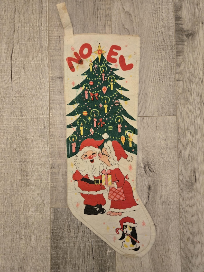 May include: A vintage Christmas stocking with a white background and a green Christmas tree with ornaments and candles. Santa Claus and Mrs. Claus are kissing under the tree. The stocking has the word "NOEL" printed in red letters.