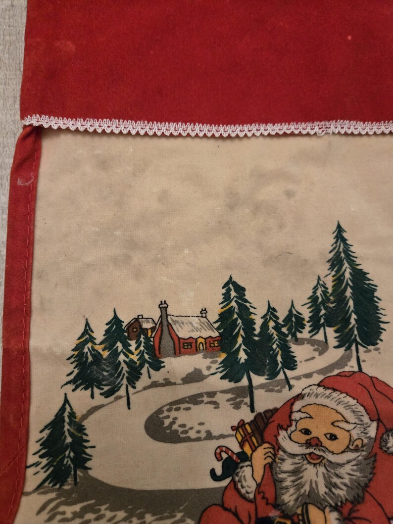 May include: A vintage Christmas stocking with a red felt top and a white lace trim. The stocking features a printed scene of Santa Claus in a snowy forest with a small house in the background.