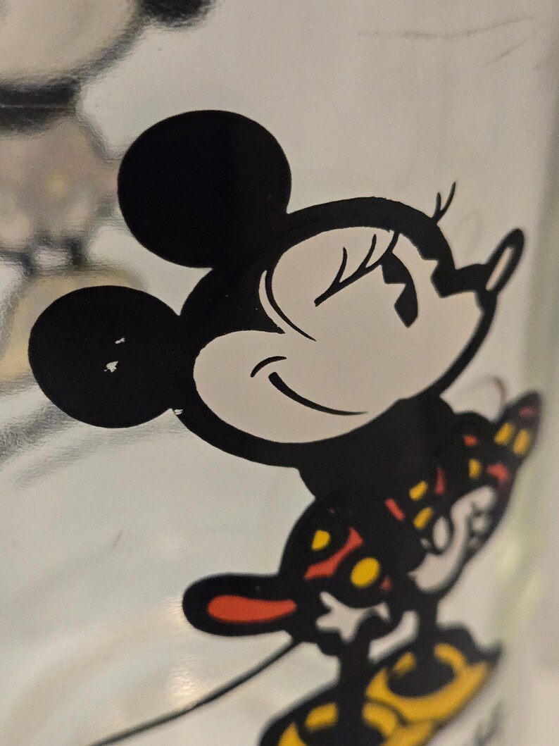 May include: A clear glass surface featuring a black and white graphic illustration of a cartoon mouse character with large round ears. The character is wearing a patterned outfit with red and yellow accents, depicted in a side profile view.