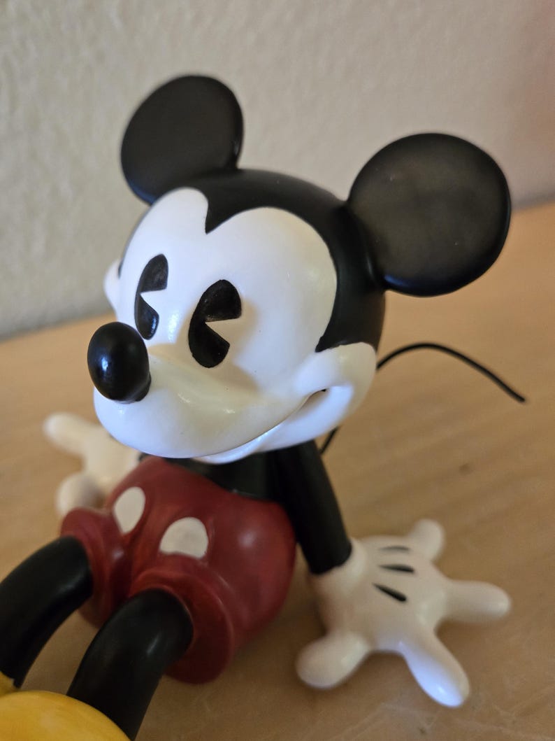 Puede incluir: Figura de Mickey Mouse con cabeza y orejas negras, cara blanca y pantalones cortos rojos. La figura tiene guantes blancos y piernas y brazos negros. Un personaje cl&aacute;sico de Disney.