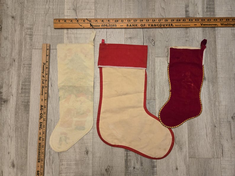 May include: Three vintage Christmas stockings. One is white with a red cuff and a printed design. Another is white with a red cuff and a plain design. The third is red velvet with a gold trim.
