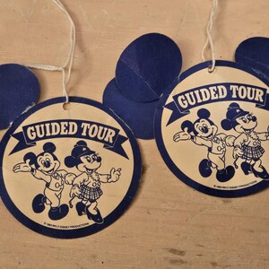 Peut inclure: Anciennes &eacute;tiquettes "Guided Tour" de Disney avec Mickey et Minnie Mouse. Les &eacute;tiquettes sont circulaires avec des d&eacute;coupes d'oreilles bleues de Mickey Mouse et les mots "Guided Tour" dans une banni&egrave;re. Les personnages sont en noir et blanc.