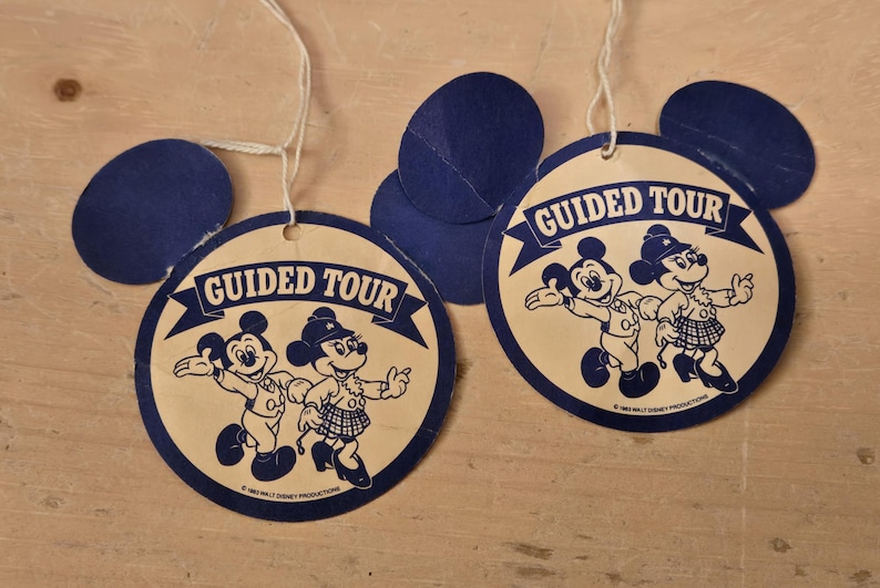 Peut inclure: Anciennes &eacute;tiquettes "Guided Tour" de Disney avec Mickey et Minnie Mouse. Les &eacute;tiquettes sont circulaires avec des d&eacute;coupes d'oreilles bleues de Mickey Mouse et les mots "Guided Tour" dans une banni&egrave;re. Les personnages sont en noir et blanc.