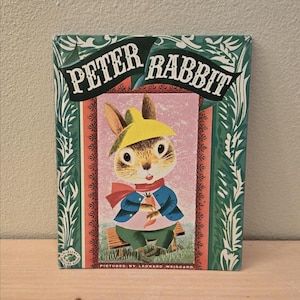 May include: A vintage children's book titled "Peter Rabbit." The cover features an illustration of Peter Rabbit wearing a yellow hat, blue jacket, and green pants, holding a carrot. The book has a green and red border with the title in white.