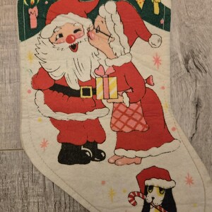 May include: A vintage Christmas stocking with a red and white illustration of Santa Claus and Mrs. Claus kissing under a green Christmas tree. A small dog with a candy cane is in the bottom corner.