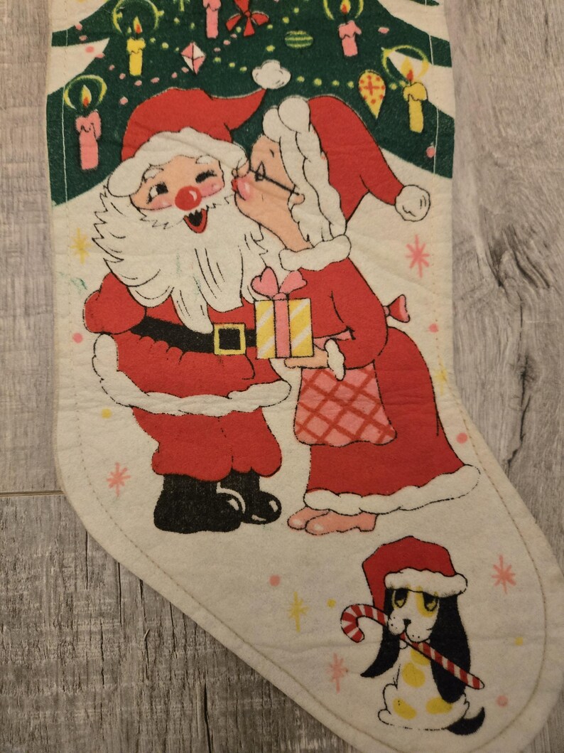 May include: A vintage Christmas stocking with a red and white illustration of Santa Claus and Mrs. Claus kissing under a green Christmas tree. A small dog with a candy cane is in the bottom corner.
