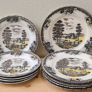 May include: Set of 9 vintage brown and white ceramic plates with a country scene design. The plates feature a brown and white farmhouse, trees, and a fence. The plates have a black and white border.