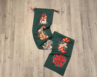 Puede incluir: Un camino de mesa navideño verde con diseños bordados. El camino presenta un muñeco de nieve, un calcetín, un bastón de caramelo y una flor de pascua. Los diseños son en rojo, blanco, amarillo y verde.