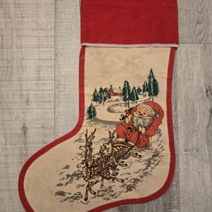 May include: A vintage Christmas stocking with a red cuff and a white background. The stocking features a printed image of Santa Claus riding in a sleigh pulled by reindeer through a snowy forest.