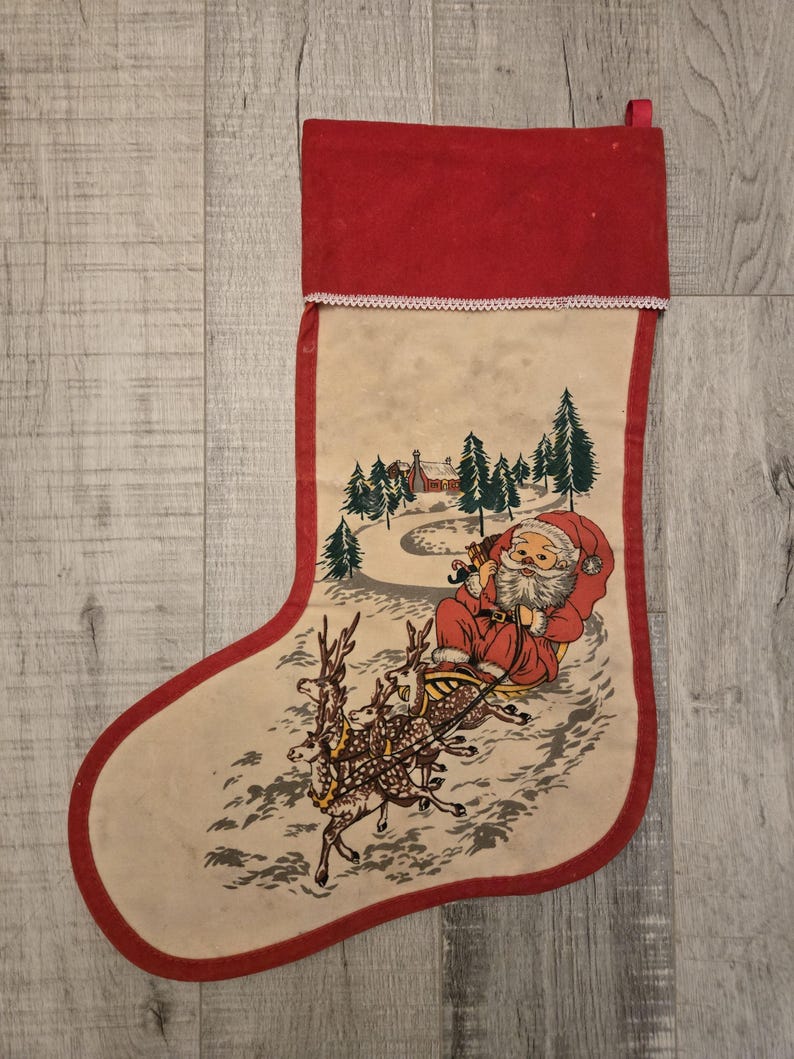 May include: A vintage Christmas stocking with a red cuff and a white background. The stocking features a printed image of Santa Claus riding in a sleigh pulled by reindeer through a snowy forest.