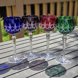 May include: Four crystal wine glasses with cut glass designs. The glasses are blue, purple, red, and green.