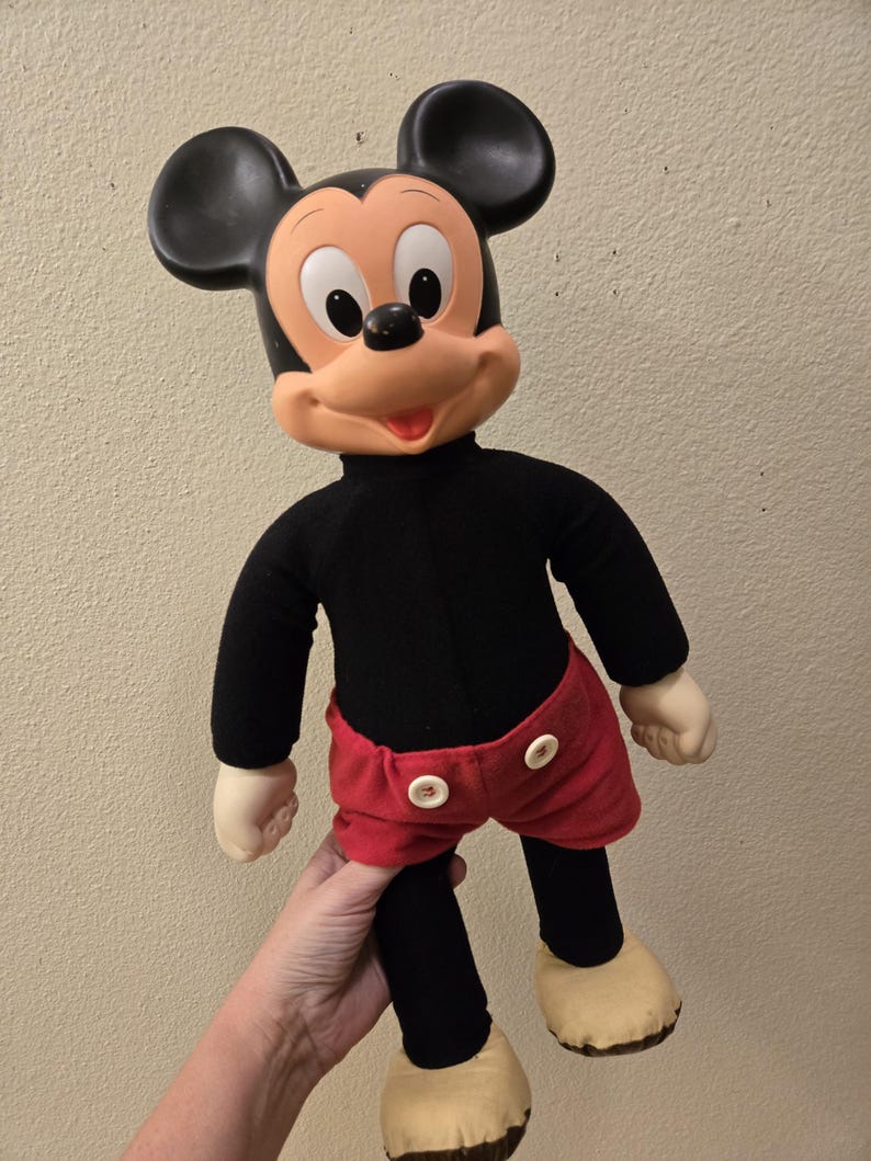 Peut inclure: Une poup&eacute;e en peluche vintage de Mickey Mouse. La poup&eacute;e a une t&ecirc;te noire avec de grandes oreilles, un visage beige et un col roul&eacute; noir. Elle porte un short rouge avec des boutons blancs, des jambes noires et des chaussures beiges.