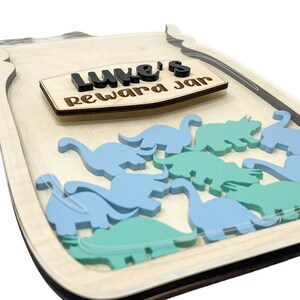 May include: Wooden reward jar with a clear plastic window, featuring the name "Luke's Reward Jar" and blue and green dinosaur shapes inside.