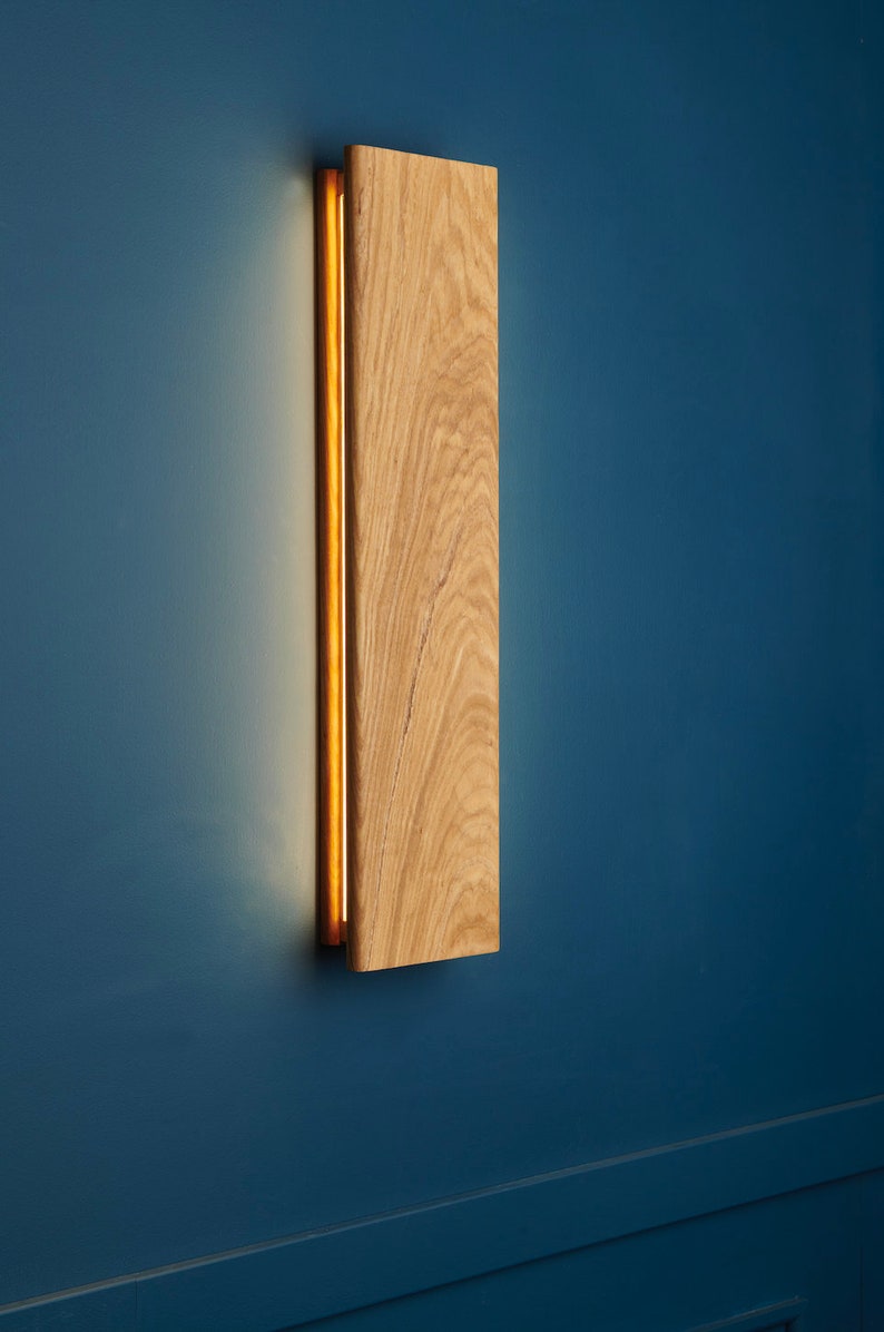 May include: A wooden wall sconce with a warm, glowing light emanating from a thin slit in the wood. The sconce is mounted on a blue wall.