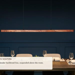 May include: A linear pendant light fixture featuring a long, slender piece of natural hardwood with a visible grain, suspended horizontally by two thin black cables. The text "QUIETLY SCULPTURAL A slender hardwood line, suspended above the room." is visible.