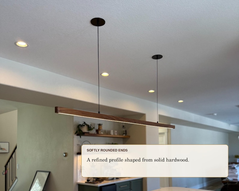 May include: A linear pendant light fixture featuring a long, horizontal bar made of dark brown solid hardwood with softly rounded ends. The fixture is suspended from the ceiling by two thin black cables and includes an integrated LED light strip.